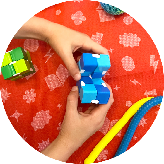 Two small hands play with a blue fidget block with other fidget toys placed on a table