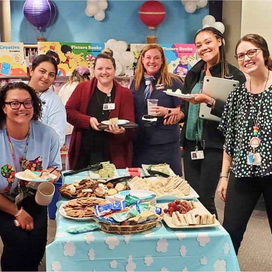 A group of smiling teachers around a snack table at a Book Fair teacher event