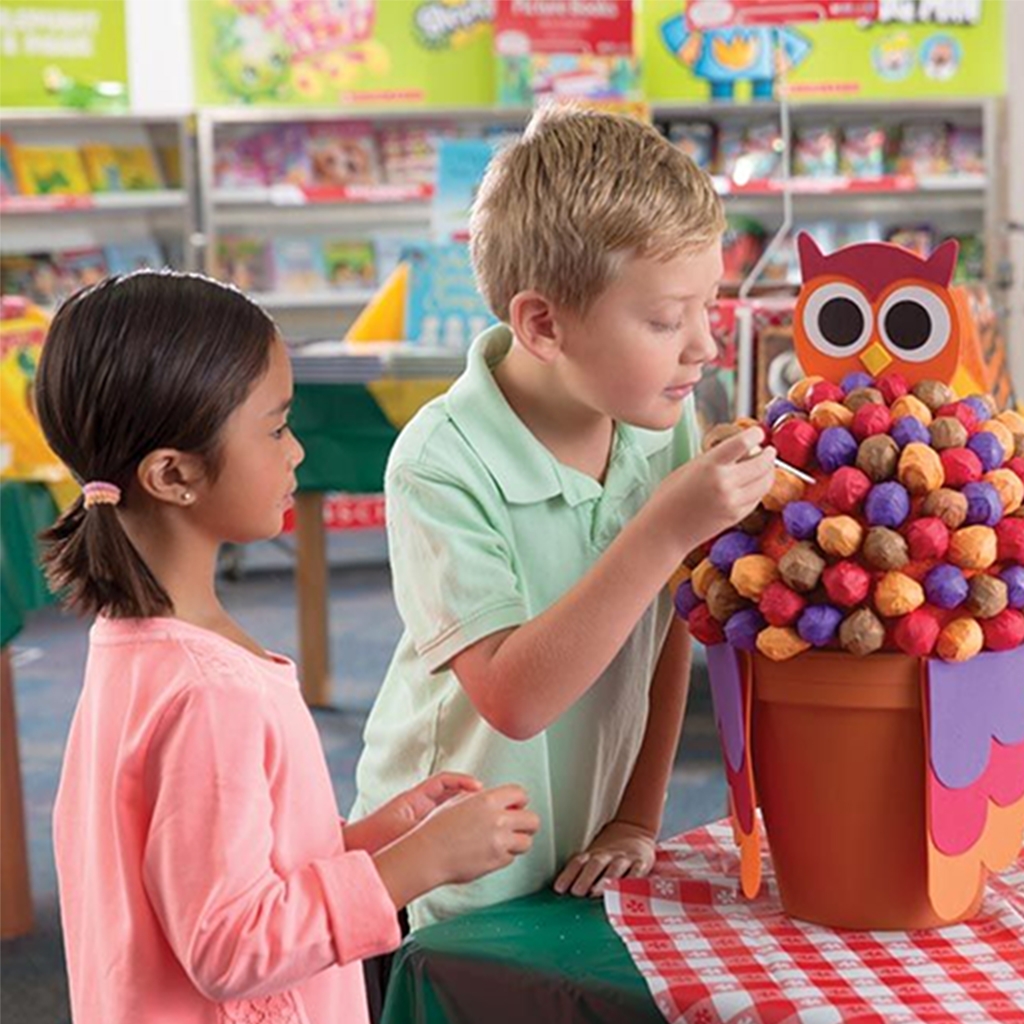 Two children pull lollipops from an owl themed basket near their Book Fair checkout