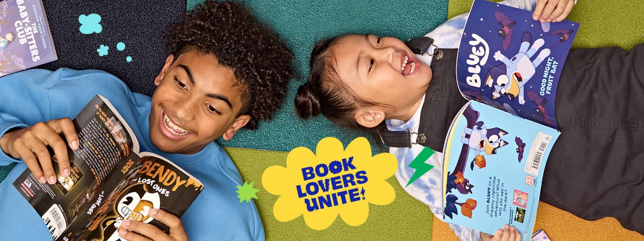 Two students lay on the ground smiling and reading Book Fair books