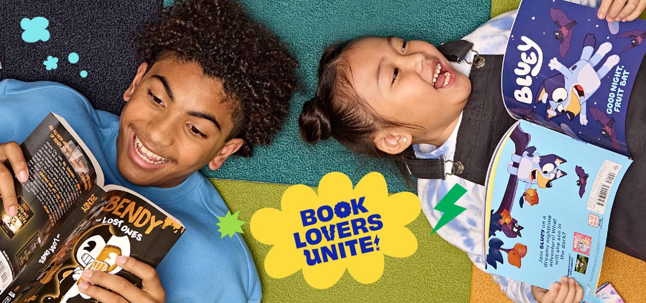 Two students lay on the ground smiling and reading Book Fair books