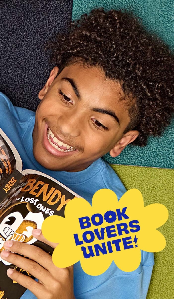 Two students lay on the ground smiling and reading Book Fair books