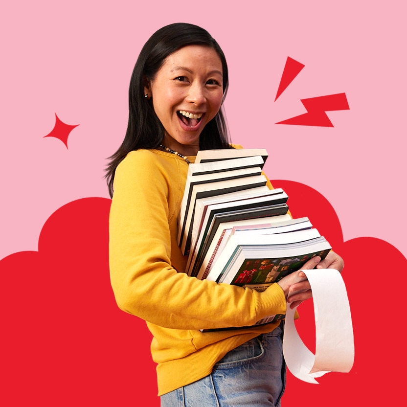 A teacher smiles brightly while holding a large pile of books 