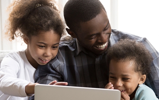 A parent and two children smile while browsing a computer screen together 