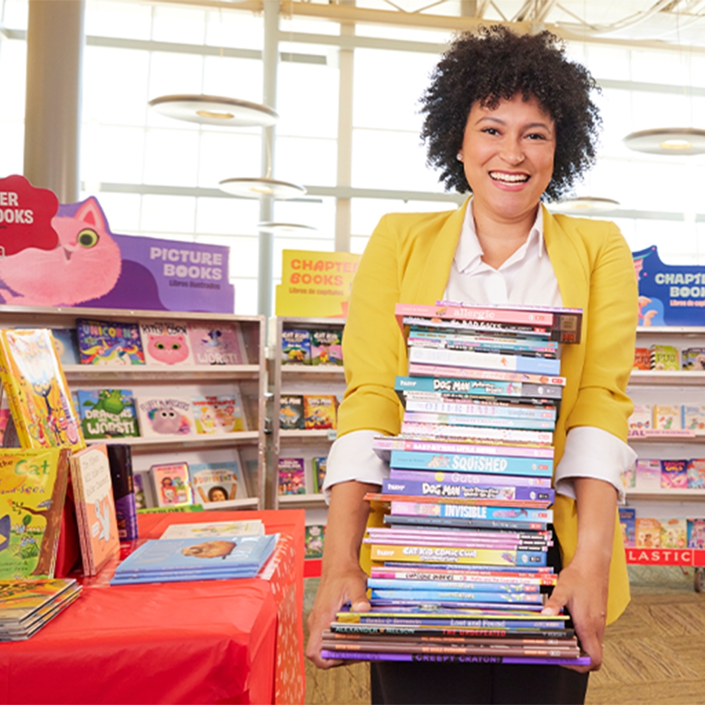 A Host carries a large stack of Books in front of their Book Fair